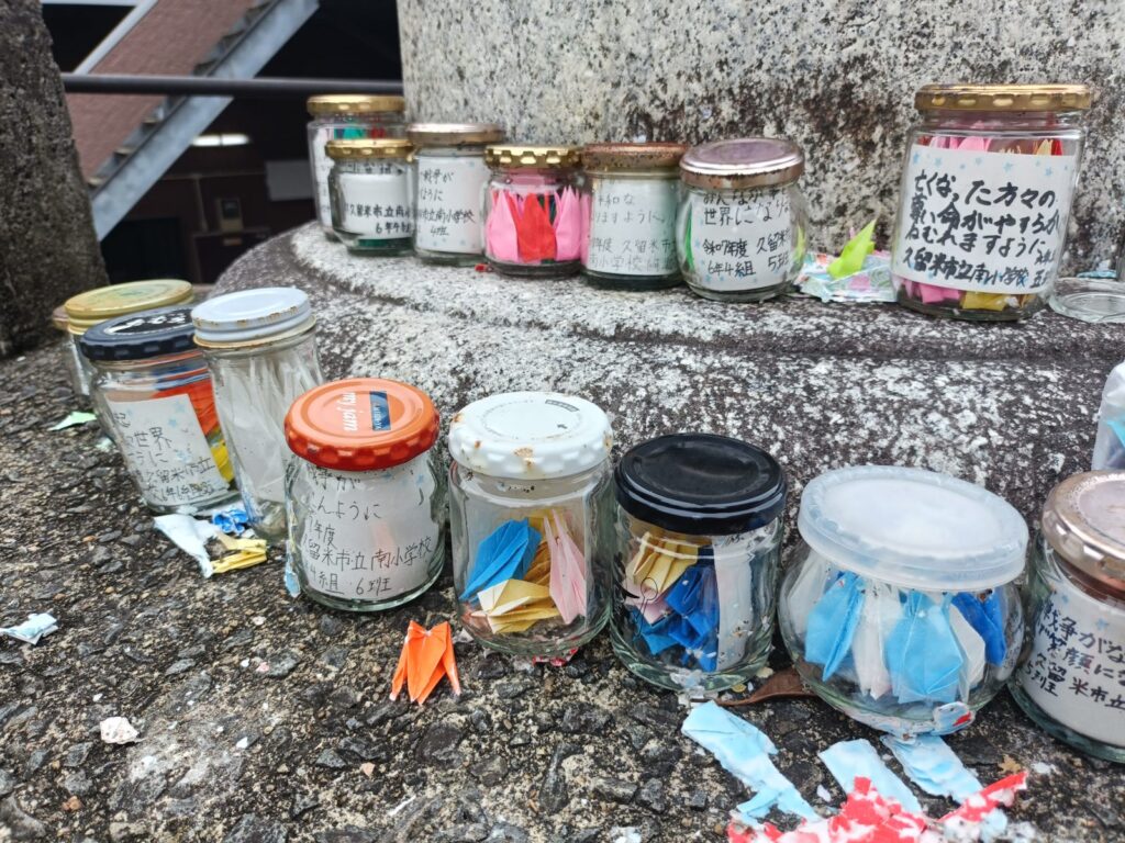 What Happens in Nagasaki on August 9: Inside the Moment of Silence at Sannō Shrine Small hand-painted jars at the base of the torii, each carrying a peace wish from local schoolchildren