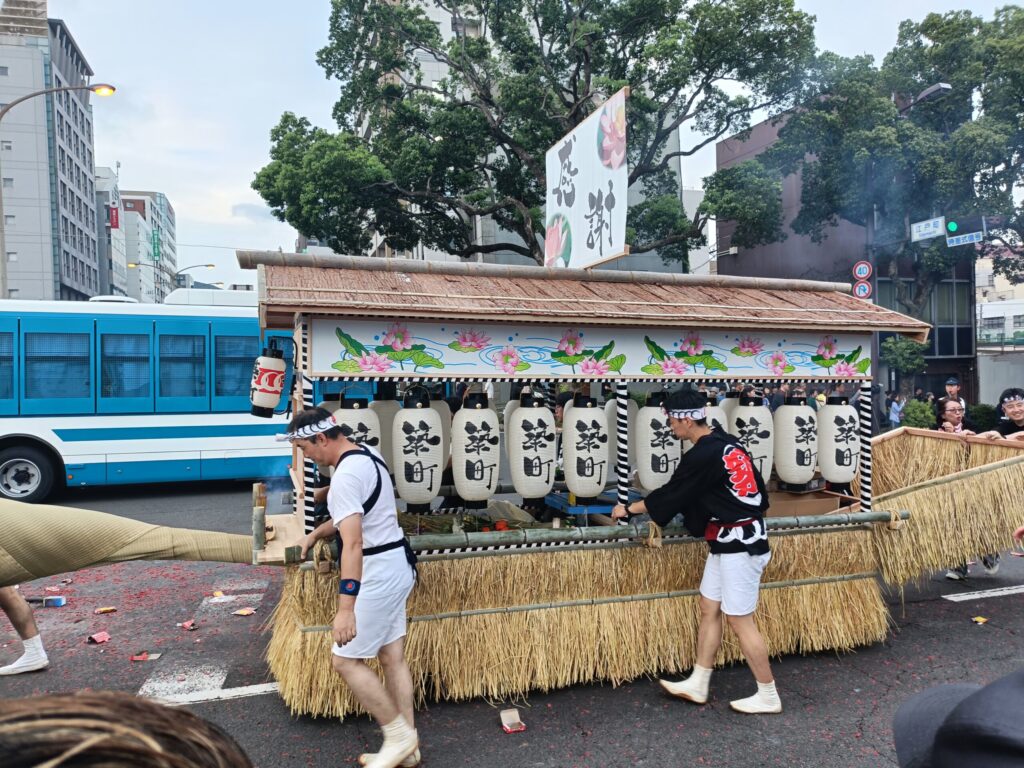 One Night a Year, Firecrackers Take Over the Streets: Nagasaki's Shoro Nagashi A moyai-bune shared spirit boat labeled "Tsuki-machi" moving through the streets during Nagasaki's Shoro Nagashi