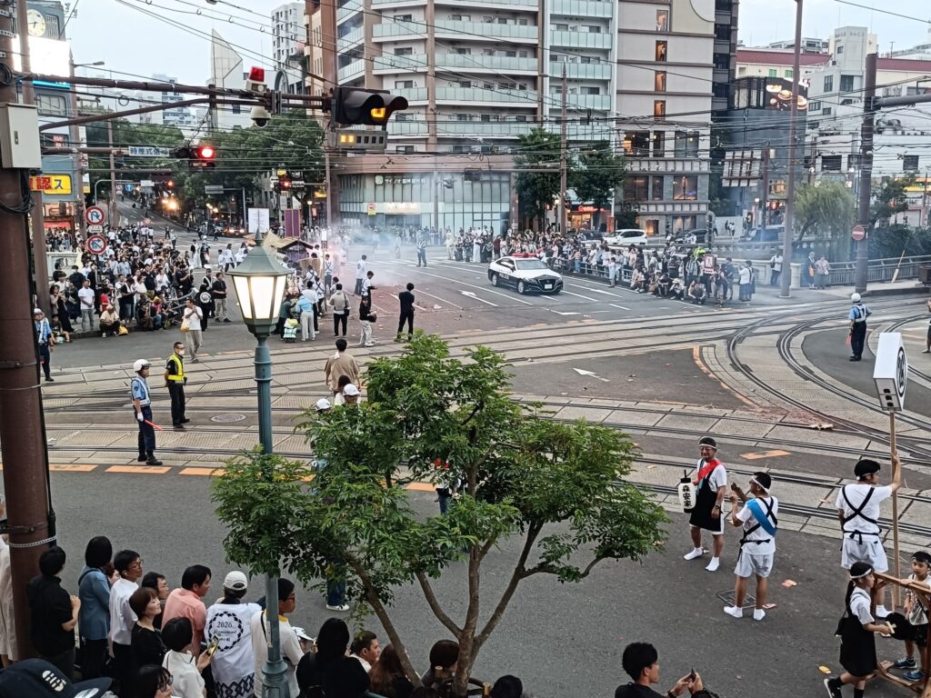 One Night a Year, Firecrackers Take Over the Streets: Nagasaki's Shoro Nagashi A police officer directing traffic at an intersection on the way to Kencho-zaka, the street filled with firecracker smoke