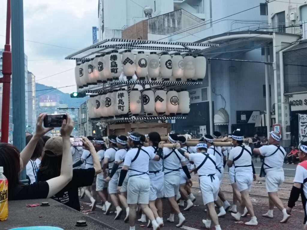 One Night a Year, Firecrackers Take Over the Streets: Nagasaki's Shoro Nagashi A spectator photographing a mikoshi-shaped spirit boat on their phone