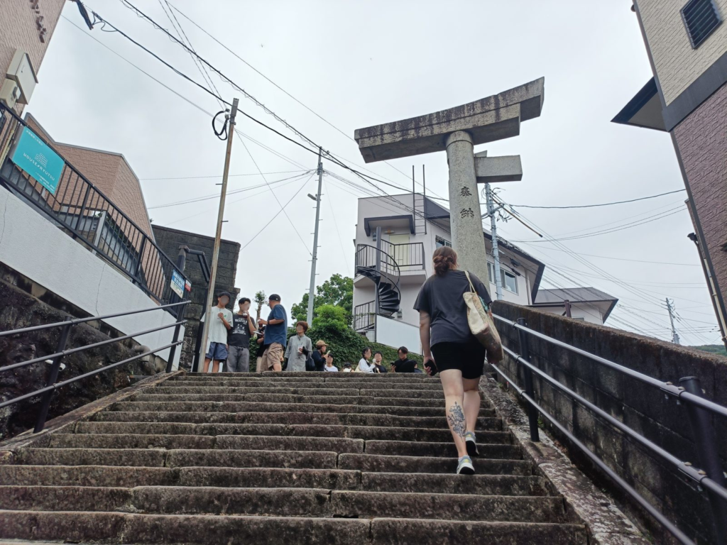 Visitors climb the stone steps toward Sannō Shrine's one-legged torii gate, its right post still standing after the 1945 atomic bombing
