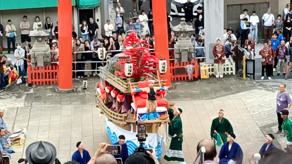 A boy standing at the bow of Aburaya-machi's kawafune float with his arms spread, during Niizoroi at Yasaka Shrine