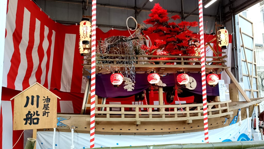 Aburaya-machi's kawafune river boat float displayed in a garage hung with red-and-white curtains during Niwamise