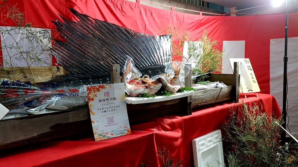 A large fish with a sail-like fin laid on ice among other fish, displayed as a gift at Aburaya-machi's Niwamise
