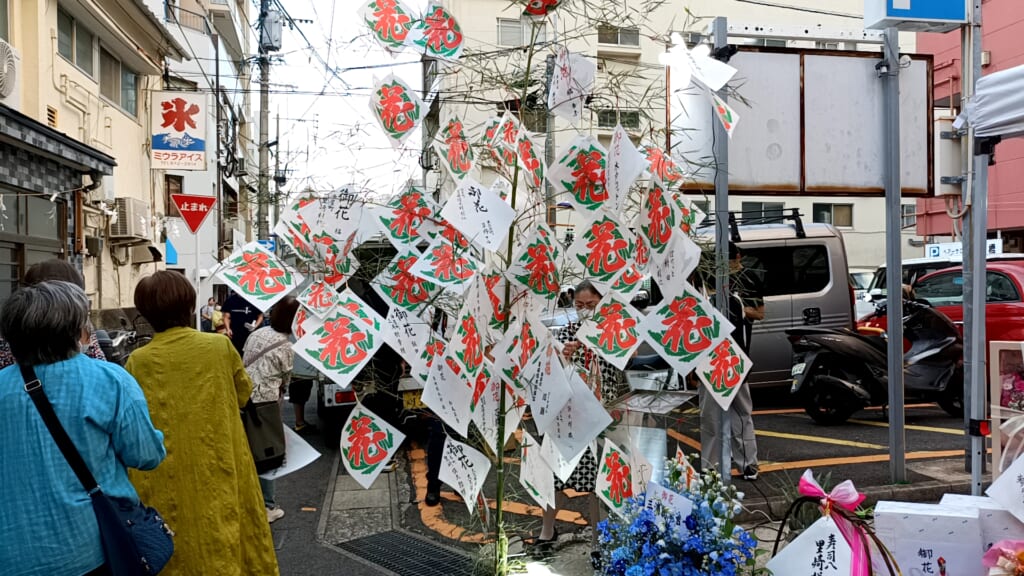 Bamboo branches hung with white paper squares printed with the red character for hana, meaning flower
